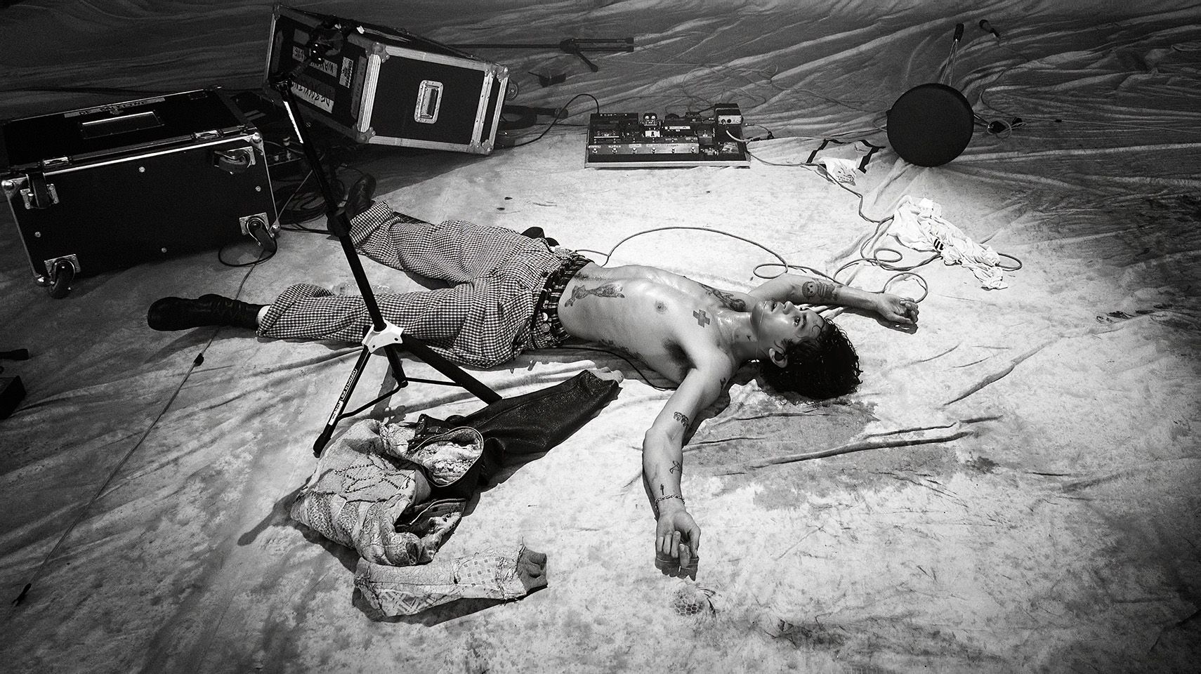 Artysta leży w samych spodniach, bez koszulki na podłodze. Dookoła niego znajdują się instrumenty muzyczne.