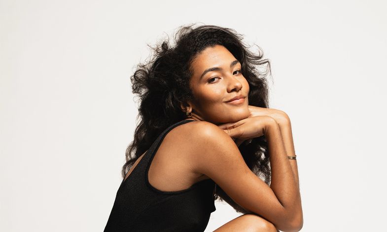 Artystka ubrana w czarną sukienkę i kozaki w panterkę pozuje na jasnym tle