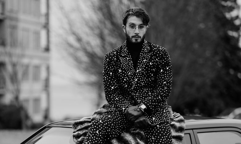 Artystas siedzi na dachu samochodu. Ubrany jest w garnitur pokryty w świecące cekiny.